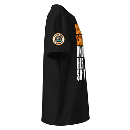 Right side view of black t-shirt showing The Tee Shop donut logo patch on the sleeve and edge of the papaya and white “BERNIE COLLINS KNOWS HER SH*T” slogan. DTF print, McLaren F1 fan style.
