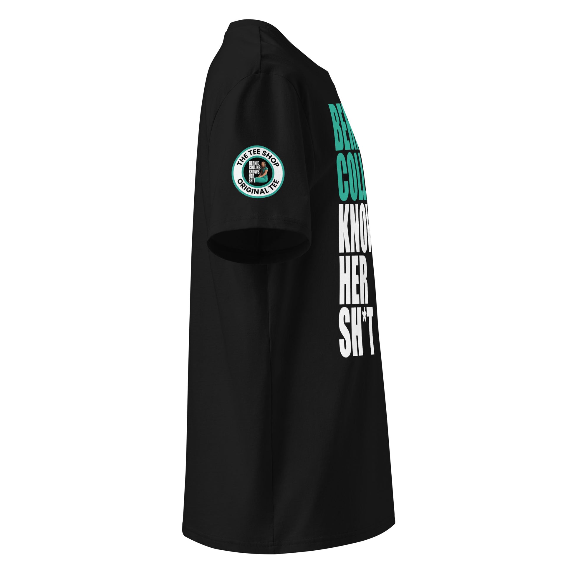 Right side view of black t-shirt showing The Tee Shop donut logo patch on the sleeve and edge of the teal and white “BERNIE COLLINS KNOWS HER SH*T” slogan. DTF print, Mercedes F1 fan style.