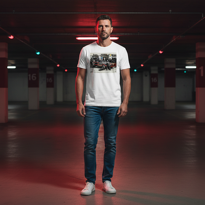 Male model wearing a white Bat Stop Graffiti T‑Shirt with a black car and red accents pit stop design, blue jeans and white trainers, standing in an underground car park with red lighting.