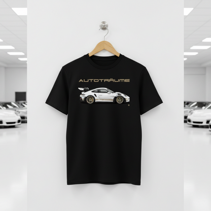 Black AUTOTRÄUME GT3 RS T-shirt featuring a white Porsche-style GT3 RS car graphic with gold details hanging on a premium wooden hanger with a silver wall peg against a central white wall panel in a bright sports car gallery with glossy white floors and blurred white and silver sports cars on both sides.