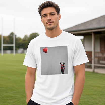 Male model wearing a white Blackheath Boy Dreams street art t-shirt featuring a stencil-style boy in Blackheath rugby club colours reaching for a red heart balloon, photographed at a rugby ground on match day