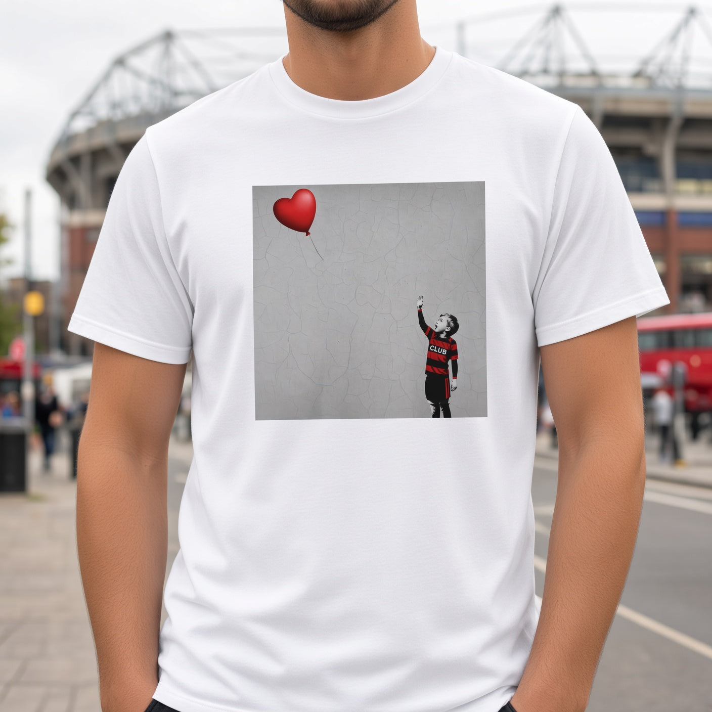 Male model wearing a white Blackheath Boy Dreams street art t-shirt with a stencil-style boy in Blackheath club colours reaching for a red heart balloon, photographed in a match day street setting