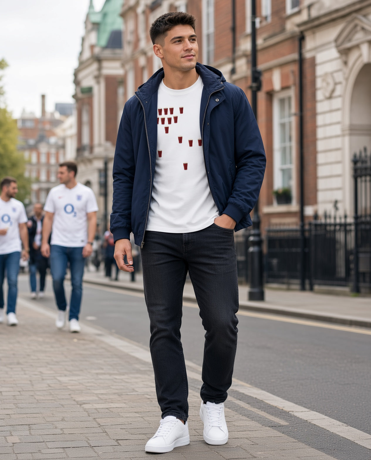 Full-length photo of a male model wearing a white Blackheath Team Pints rugby t-shirt with scattered red and black pint graphics, walking on a London street in a match day crowd setting