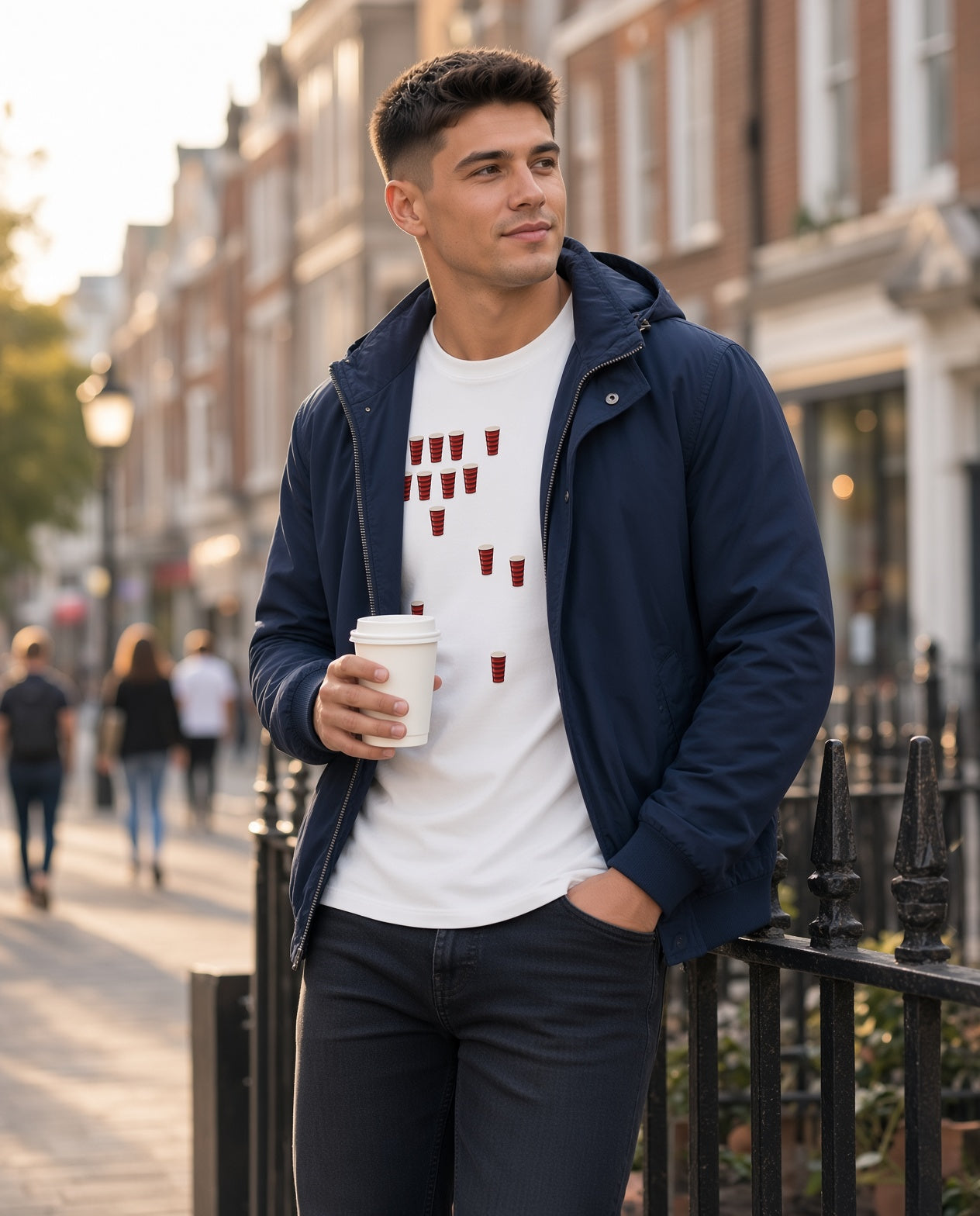 Male model wearing a white Blackheath Team Pints rugby t-shirt with multiple small red and black striped pint graphics, styled with a jacket on a London street for match day supporters
