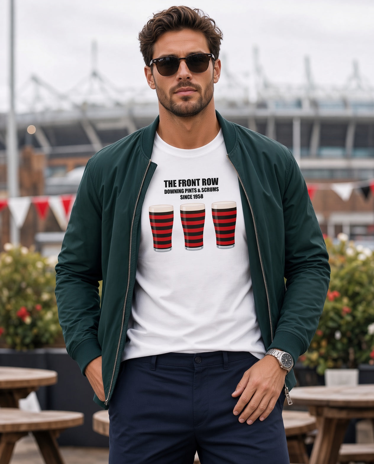 Male model wearing a white Blackheath rugby t-shirt that reads “The Front Row – Downing Pints & Scrums Since 1858” with three red and black pint graphics, styled with a jacket for match day fanwear