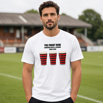 Male model wearing a white Blackheath rugby t-shirt reading “The Front Row - Downing Pints & Scrums Since 1858” with three red and black pint graphics, photographed at a rugby ground for match day supporters