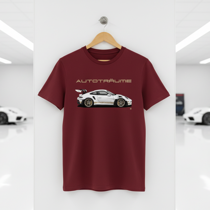 Burgundy unisex organic cotton AUTOTRÄUME GT3 RS T-shirt featuring a large, centred white Porsche-style GT3 RS car graphic with gold details hanging on a premium wooden hanger with a silver wall peg against a clean white wall panel in a bright modern sports car gallery with glossy floors and blurred white and silver sports cars on both sides.