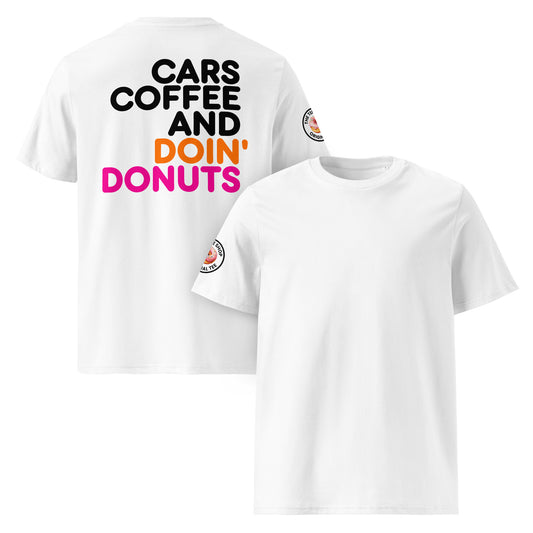 White unisex t-shirt with a plain front, bold “Cars Coffee and Doin’ Donuts” slogan in black, orange, and pink Impact font printed large on the back, and The Tee Shop circular donut logo patch on the right sleeve. DTF printed, minimalist car meet tee for petrolheads who love a statement back print and clean style.