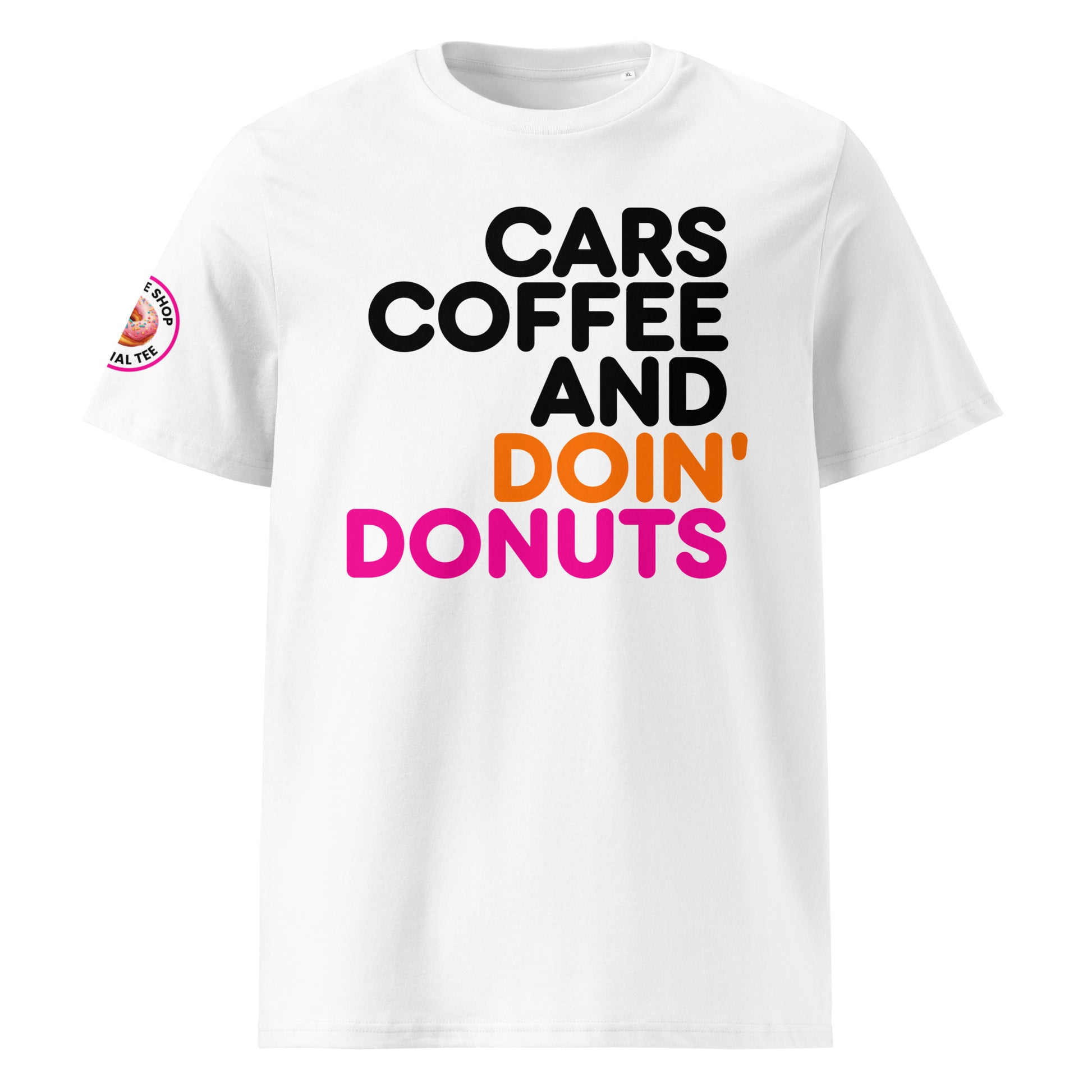 White unisex t-shirt with bold “Cars Coffee and Doin’ Donuts” slogan in black, orange, and pink Impact font. The Tee Shop donut logo patch on right sleeve. Perfect for car meets and coffee runs.
