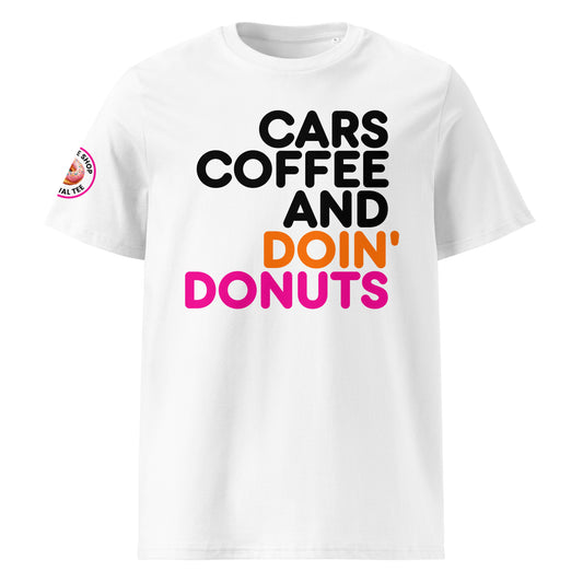 White unisex t-shirt with bold “Cars Coffee and Doin’ Donuts” slogan in black, orange, and pink Impact font. The Tee Shop donut logo patch on right sleeve. Perfect for car meets and coffee runs.