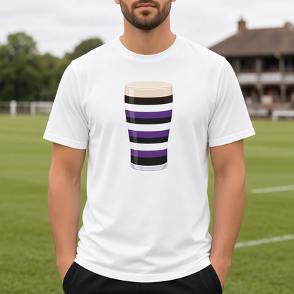 Close-up of the Terenure Mega Pint rugby t-shirt design on a white tee, showing the purple, black and white striped pint glass graphic for Terenure College supporters. Background shows a  rugby club pavilion