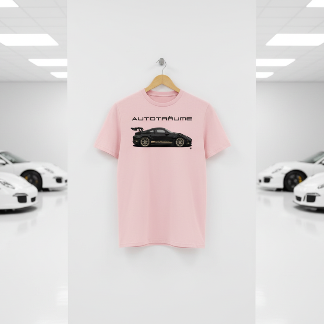 Soft cotton pink AUTOTRÄUME GT3 T‑shirt with a black Porsche‑style car and gold highlights illustration hanging on a premium wooden hanger and silver wall peg against a central white wall in a bright sports car gallery, with a glossy white floor and blurred white and silver sports cars running down both sides.