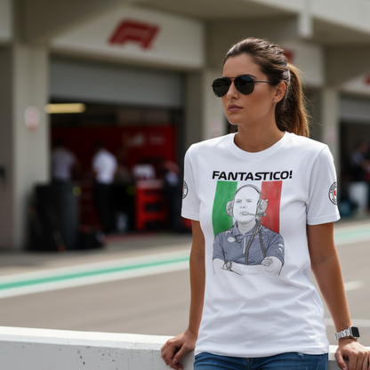 Female motorsport fan in sunglasses leaning on a pit wall barrier wearing a white FANTASTICO! GP race engineer T‑shirt with Italian flag background and FANTASTICO text, with garages and pit lane blurred behind.