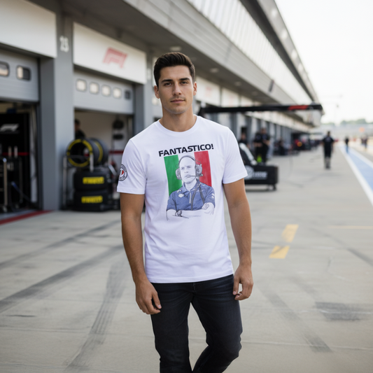 Male F1 fan in the paddock wearing a white FANTASTICO! GP race engineer T‑shirt with Italian flag background and FANTASTICO text, standing near the pit wall and garages.