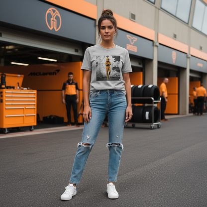 Female model wearing the heather grey organic cotton Papaya Driver Mood Graffiti Art F1 T-Shirt featuring a McLaren-inspired driver in vibrant papaya orange graffiti, standing with arms relaxed by her sides in a Papaya F1 paddock environment.