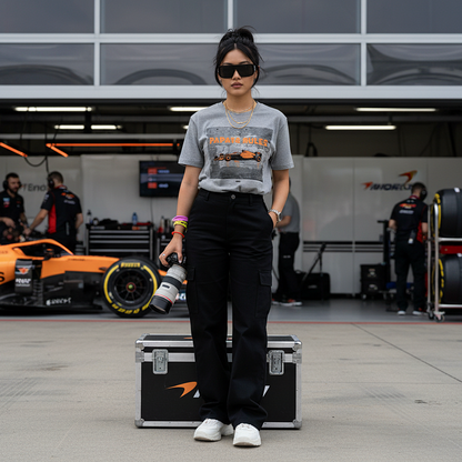 Female model wearing the heather grey organic cotton Papaya Rules 2.0 graffiti art F1 t-shirt without a jacket, styled casually in a motorsport paddock environment with motorsport props.