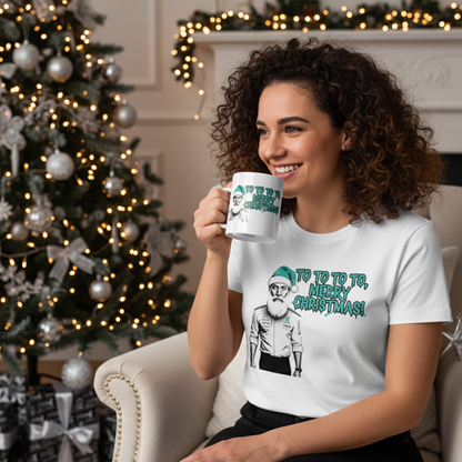 Female model wearing the white Toto Wolff Merry Christmas T-Shirt and holding the matching mug, in a Christmas-themed setting with Mercedes-AMG F1 fan decorations and a holiday tree.