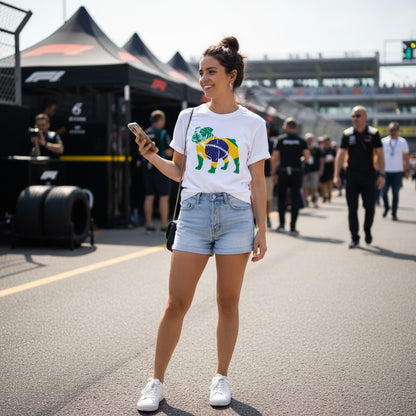 Smiling young woman wearing TheTeeShop’s Forever Roscoe Hamilton Brazilian Flag T-Shirt from the Paddock Collection, standing in a motorsport paddock area with tents and racing teams in the background, showcasing stylish casual racing apparel.
