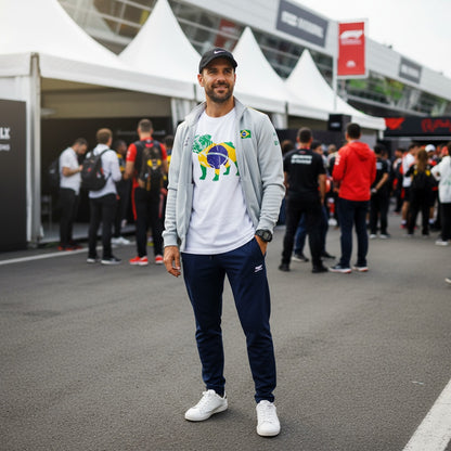 Man wearing TheTeeShop’s Forever Roscoe Hamilton Brazilian Flag T-Shirt from the Paddock Collection, standing in a busy motorsport paddock area, styled with casual sportswear and a cap, showcasing unique racing-inspired apparel.