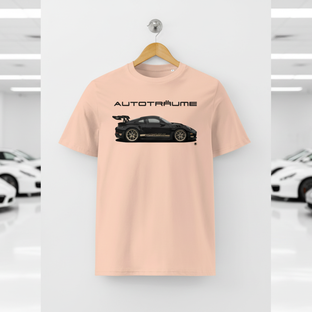 Soft peach AUTOTRÄUME GT3 T‑shirt with a black Porsche‑style car and gold highlights illustration hanging on a premium wooden hanger and silver wall peg against a central white wall in a bright sports car gallery, with a glossy white floor and blurred white and silver sports cars running down both sides.