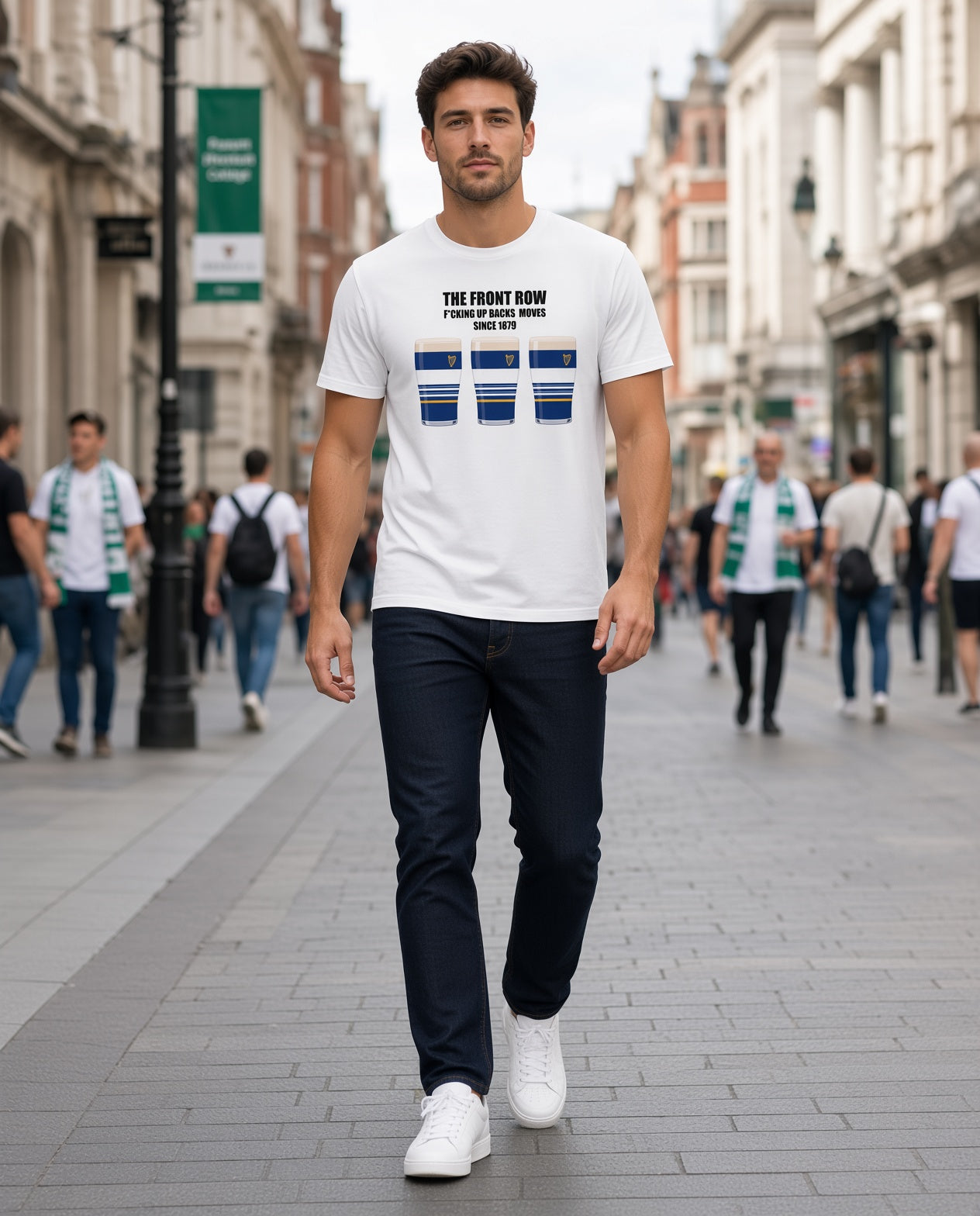 Full-length photo of a male model wearing a white Leinster rugby t-shirt reading “The Front Row - F*cking Up Backs Moves Since 1879” with three blue striped pint graphics featuring a harp crest, walking on a street with supporters in the background