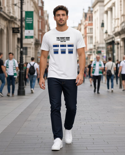 Full-length photo of a male model wearing a white Leinster rugby t-shirt reading “The Front Row - F*cking Up Backs Moves Since 1879” with three blue striped pint graphics featuring a harp crest, walking on a street with supporters in the background