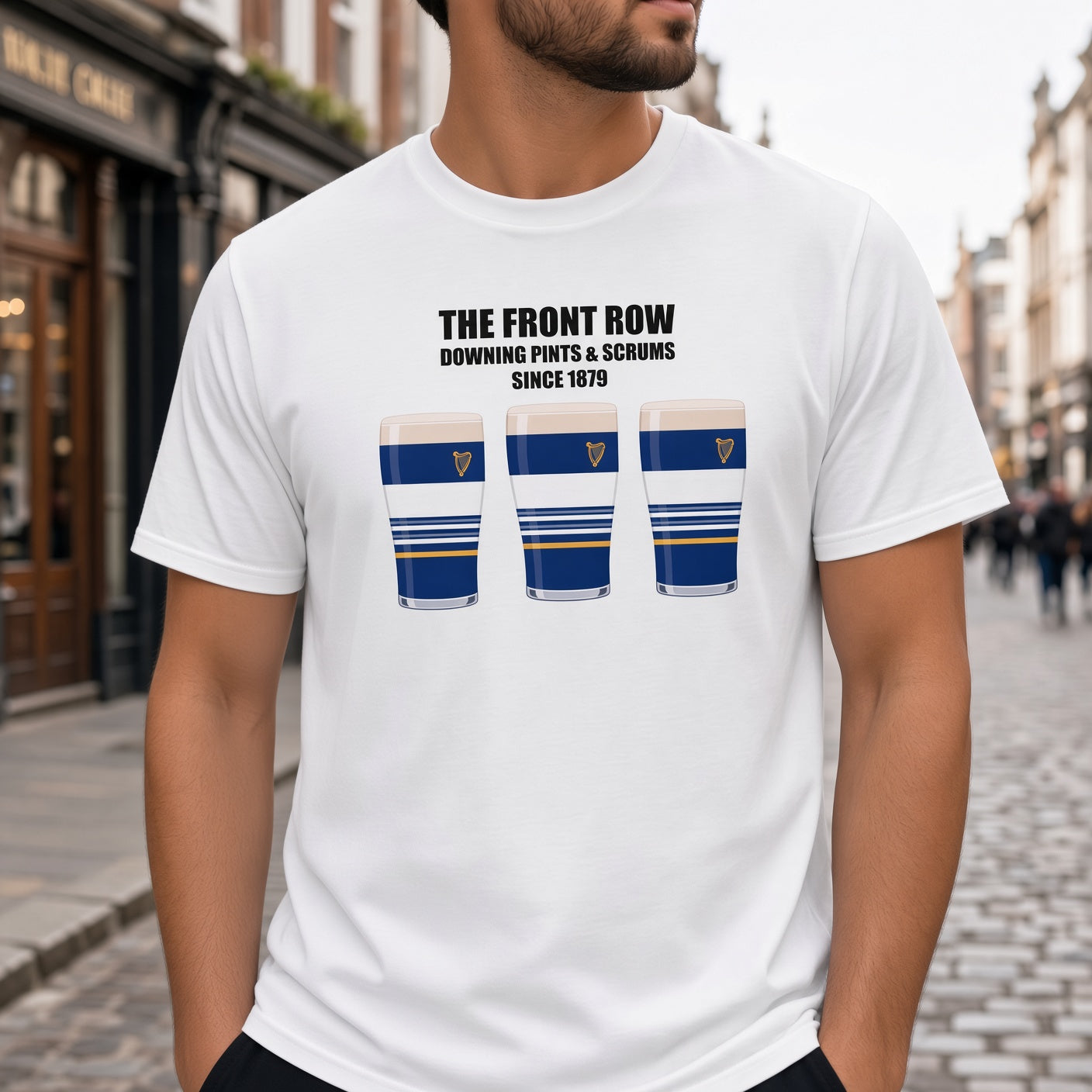 Close-up of a male model wearing a white Leinster rugby t-shirt reading “The Front Row - Downing Pints & Scrums Since 1879” with three blue striped pint graphics featuring a harp crest, photographed outdoors for match day supporters