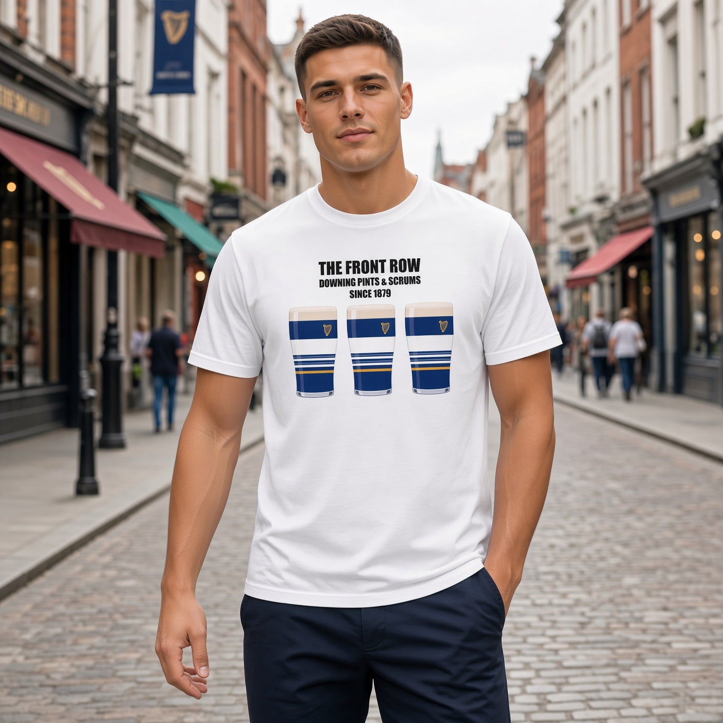 Male model wearing a white Leinster rugby t-shirt reading “The Front Row - Downing Pints & Scrums Since 1879” with three blue striped pint graphics featuring a harp crest, photographed outdoors for Leinster match day supporters