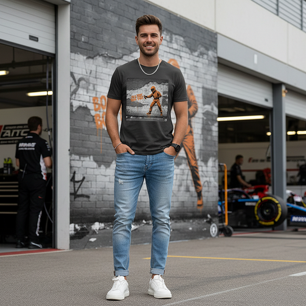 Male model wearing the anthracite organic cotton BOX BOX graffiti street art F1 t-shirt with pit crew design, styled in a motorsport paddock environment featuring a clever repeat of the graffiti image on the wall behind.