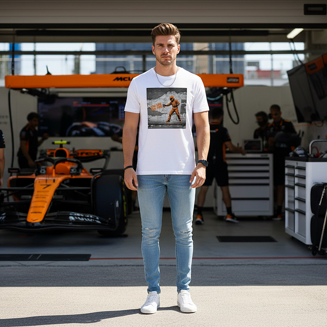 Male model wearing the white organic cotton BOX BOX graffiti street art t-shirt with a pit crew design, styled in a McLaren-themed motorsport paddock environment, tee clean and readable.
