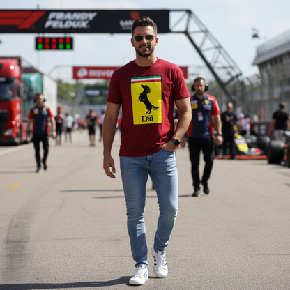 Male motorsport fan in a grand prix paddock wearing the burgundy Prancing Leo T-Shirt, featuring a yellow badge with a black dachshund silhouette and “Leo” text, perfect for racing and dog lovers.