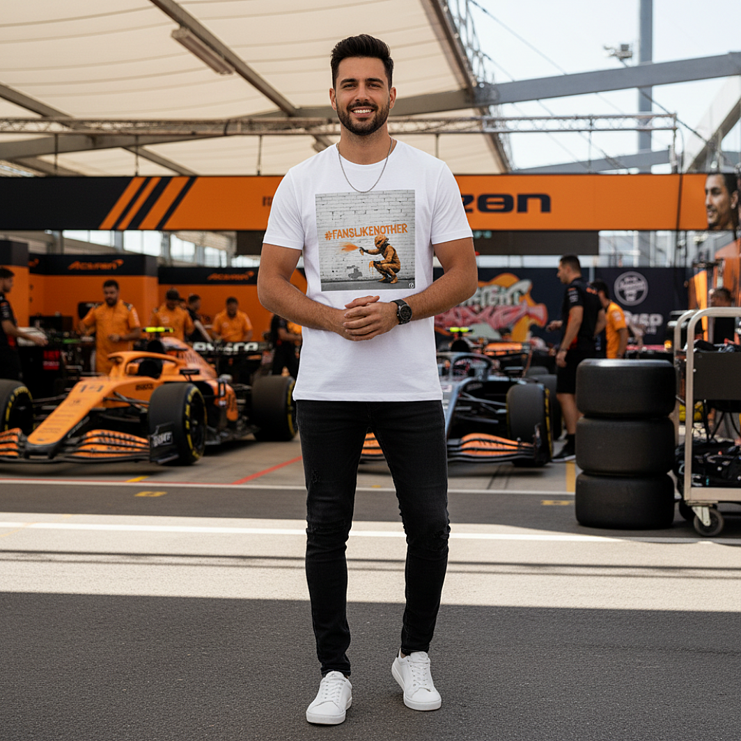 Male model wearing the white organic cotton PAPAYA Fans Like No Other Graffiti Art F1 T-Shirt with #FANSLIKENOOTHER design, standing with arms relaxed by his sides in a full-frame motorsport paddock environment, tee clean and design fully visible.