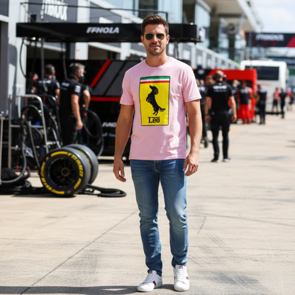 Male motorsport fan in a grand prix paddock wearing the pink Prancing Leo T-Shirt, featuring a yellow badge with a black dachshund silhouette and “Leo” text, perfect for racing and dog lovers.