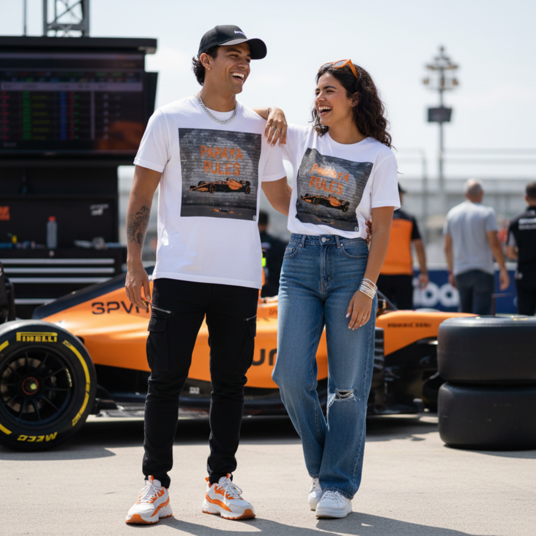 Male and female models together wearing white organic cotton Papaya Rules graffiti art t-shirts in a motorsport paddock, styled fashionably with motorsport props and a casual vibe.