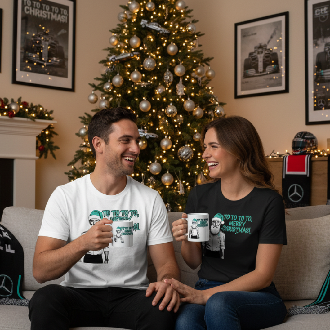 Male and female models wearing the Toto Wolff Merry Christmas T-Shirts (white and black versions) and holding the official mug, enjoying a festive scene with Mercedes F1 memorabilia and holiday decorations.