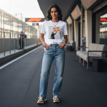 Young woman wearing TheTeeShop’s Max Series DU DU DU DU Graffiti T-Shirt, featuring Max Verstappen spray-painting his famous chant, standing in a Formula 1 paddock with team members and garages in the background, perfect for Max Verstappen supporters and F1 fans.