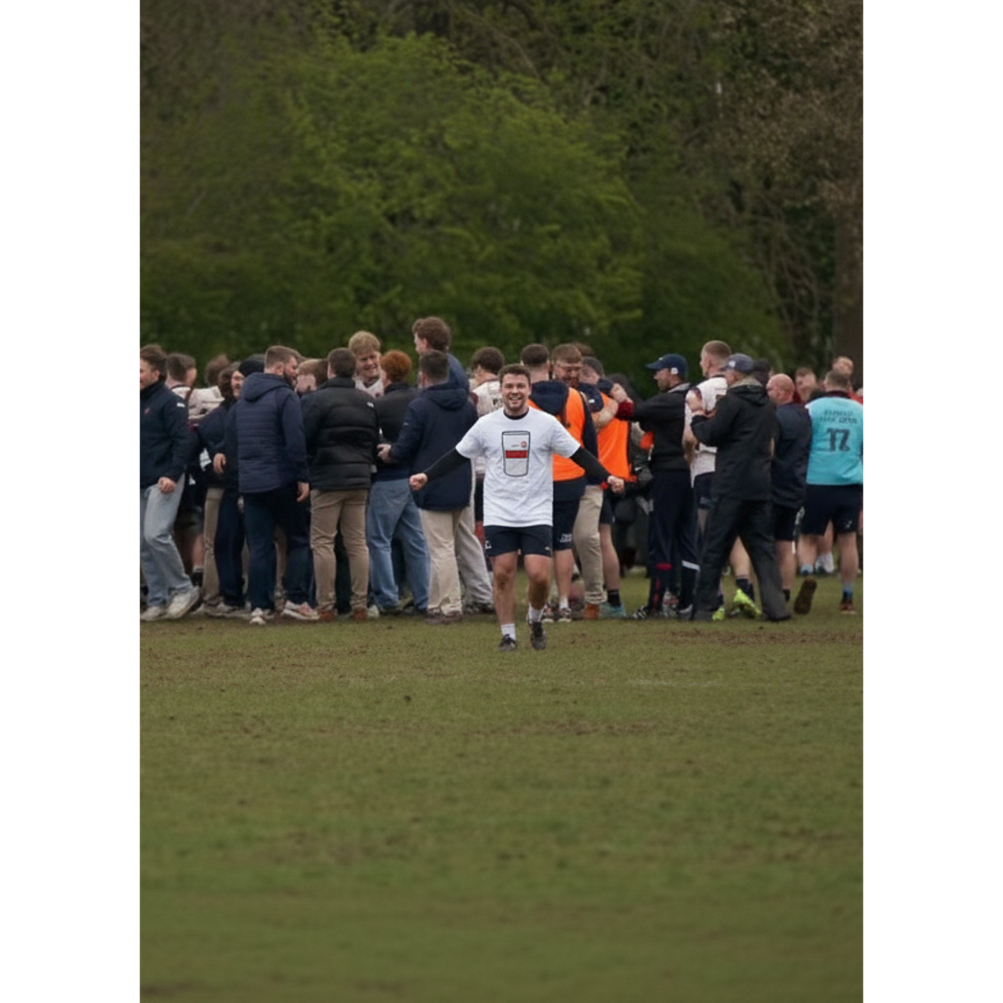 Man wearing white Old Wesley Mega Pint Rugby T-Shirt celebrating with a large group of rugby supporters and players on the pitch.