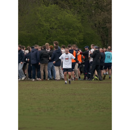 Man wearing white Old Wesley Mega Pint Rugby T-Shirt celebrating with a large group of rugby supporters and players on the pitch.