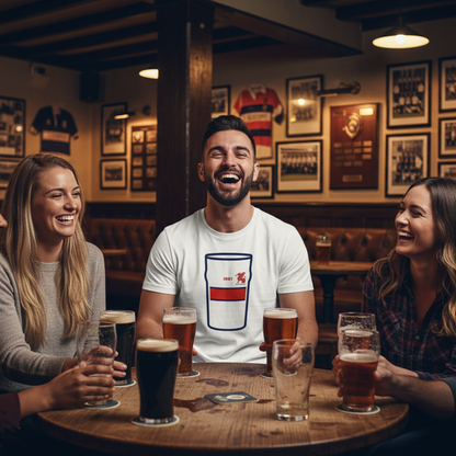 Man wearing white Old Wesley Mega Pint Rugby T-Shirt sitting with friends around a pub table with pints in a warm clubhouse setting.