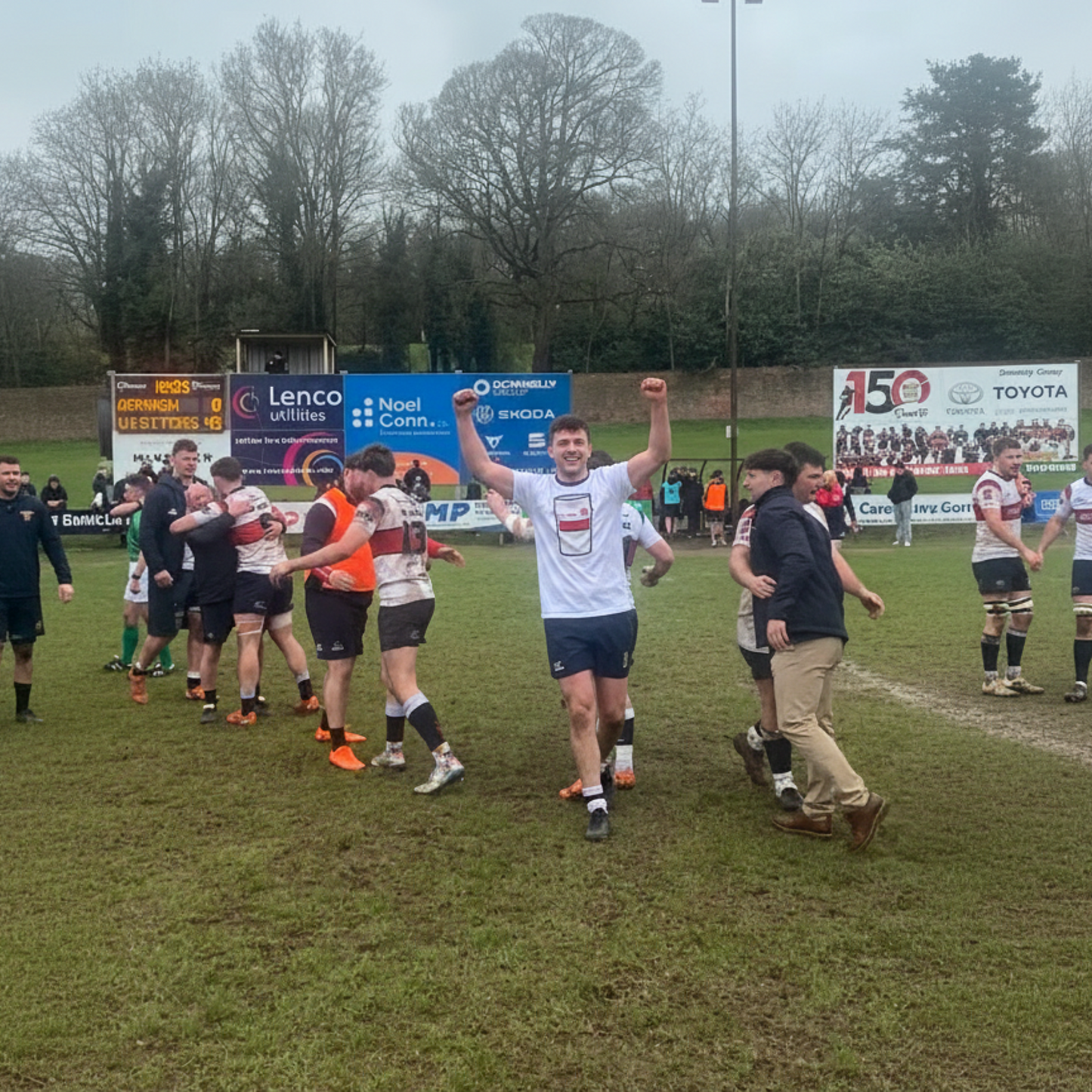 Rugby player wearing white Old Wesley Mega Pint Rugby T-Shirt celebrating with arms raised on the pitch after a match win.