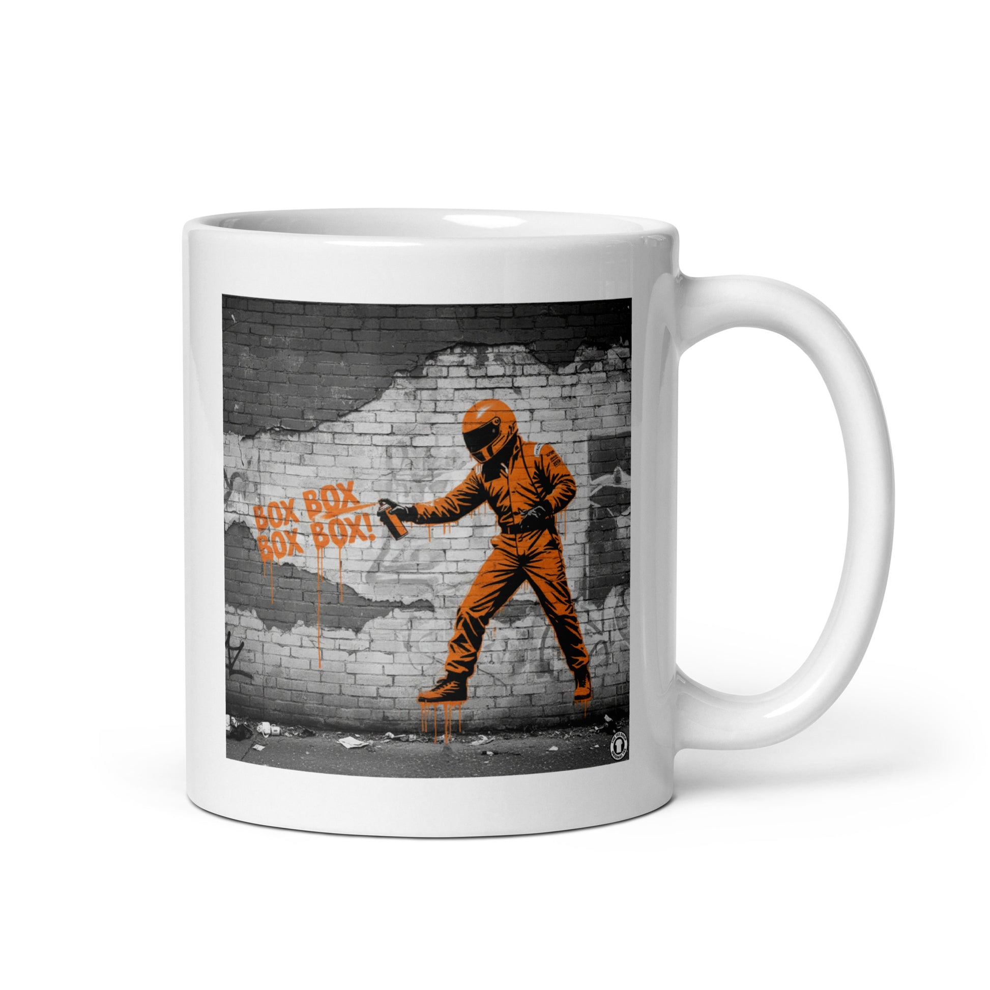 White ceramic 11oz mug featuring a street art illustration of a racing driver in a papaya suit spray-painting “BOX BOX BOX BOX!” in orange on a distressed brick wall, inspired by McLaren F1 pit stops.