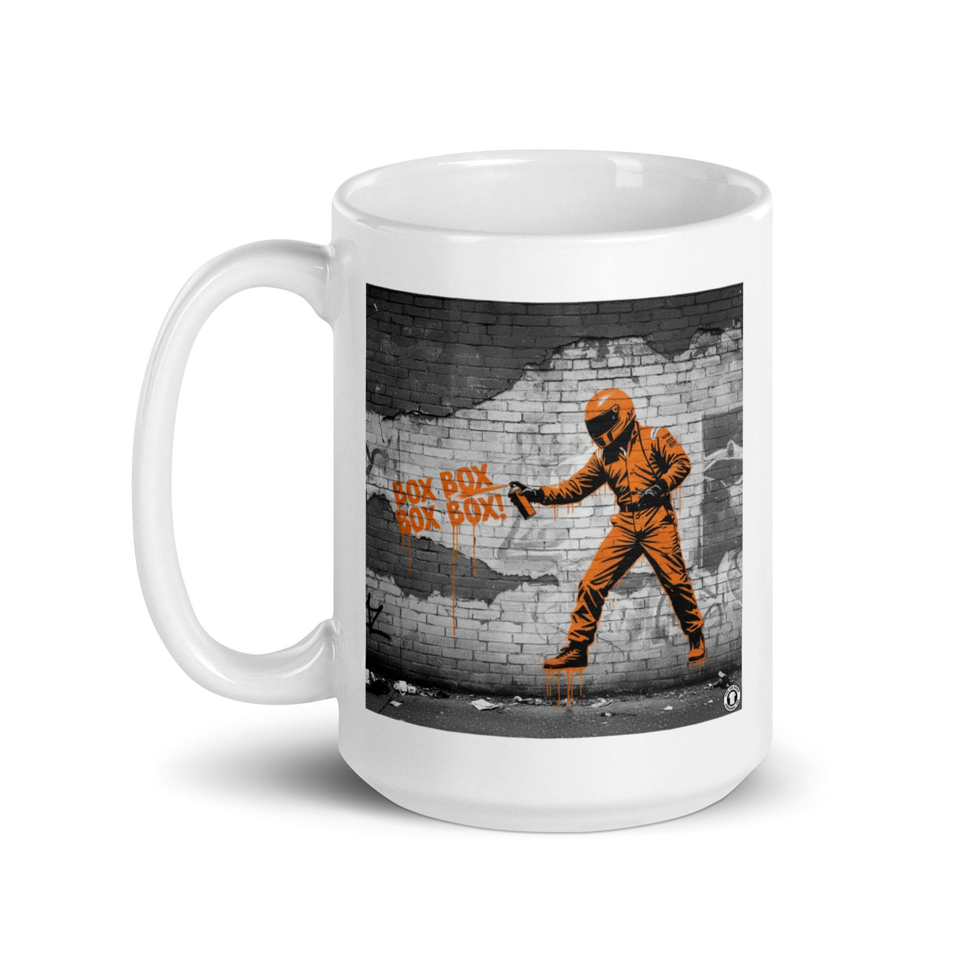 White ceramic 15oz mug featuring a street art illustration of a racing driver in a papaya suit spray-painting “BOX BOX BOX BOX!” in orange on a distressed brick wall, inspired by McLaren F1 pit stops.