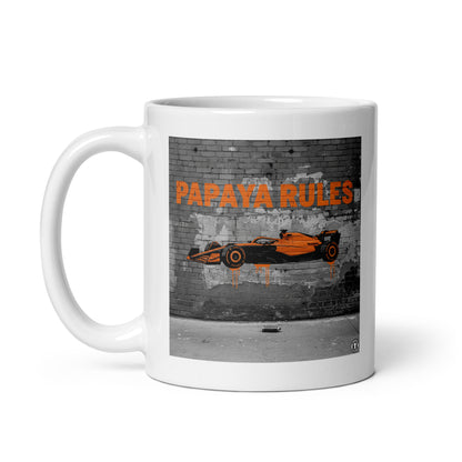 White ceramic 11oz mug featuring a street art illustration of a papaya orange McLaren F1 car and “PAPAYA RULES” graffiti on a distressed brick wall.
