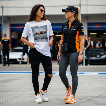 Two women chatting at a Formula 1 paddock; one wearing TheTeeShop’s Papaya Series Graffiti Racer T-Shirt and the other in official McLaren teamwear, showcasing bold McLaren-inspired motorsport streetwear.