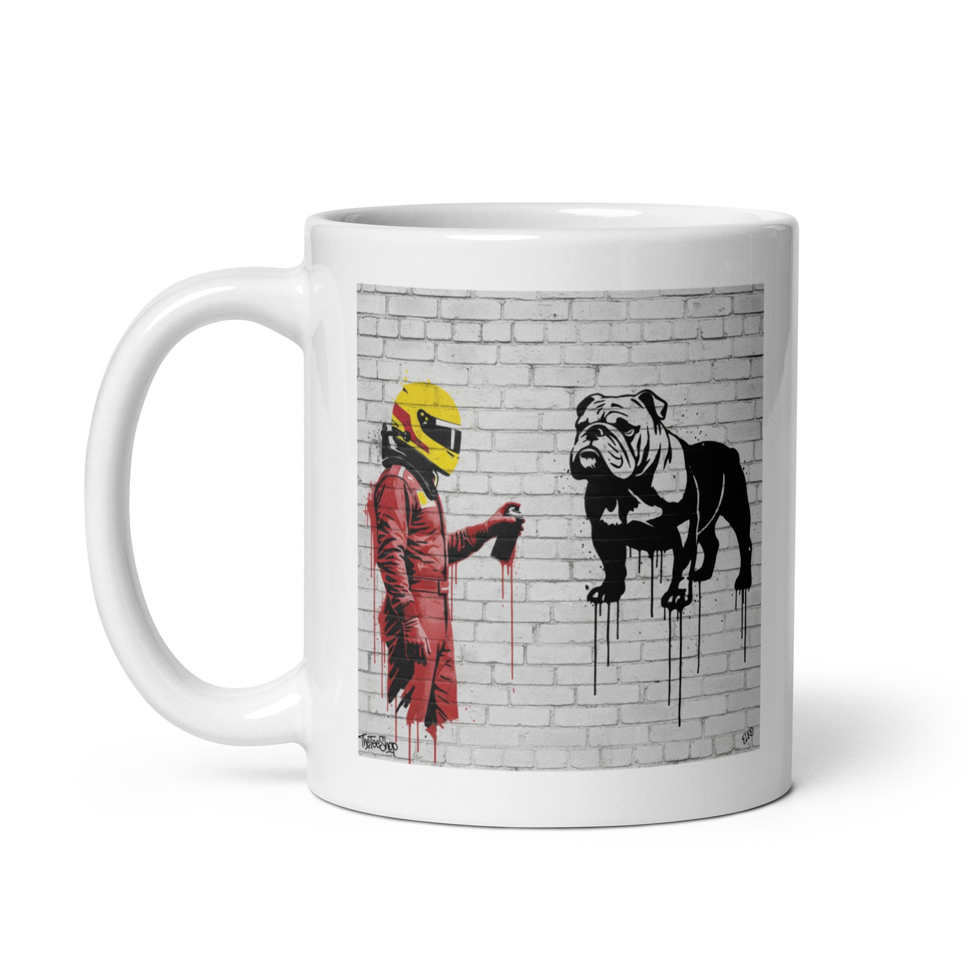 White ceramic 11oz mug featuring a street art illustration of a racing driver in red overalls and a yellow helmet spray-painting a black and white bulldog on a white brick wall.
