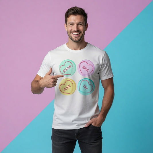 Male model wearing a white Rugby Love Hearts t‑shirt with pastel heart graphics reading Scrum, Maul, Ruck and Try