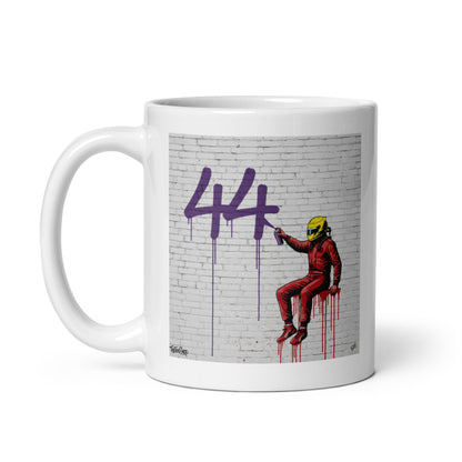 White ceramic 11oz mug featuring a street art illustration of a racing driver in Ferrari red overalls and a yellow helmet spray-painting a large purple 44 on a white brick wall, inspired by Lewis Hamilton and Ferrari.