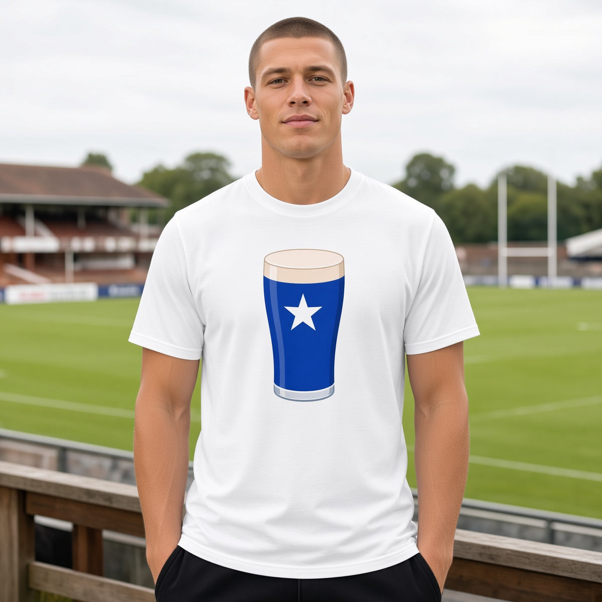 Male model wearing a white St Mary’s College Mega Pint rugby t-shirt with a blue pint glass and white star graphic, photographed at a rugby ground for match day supporters