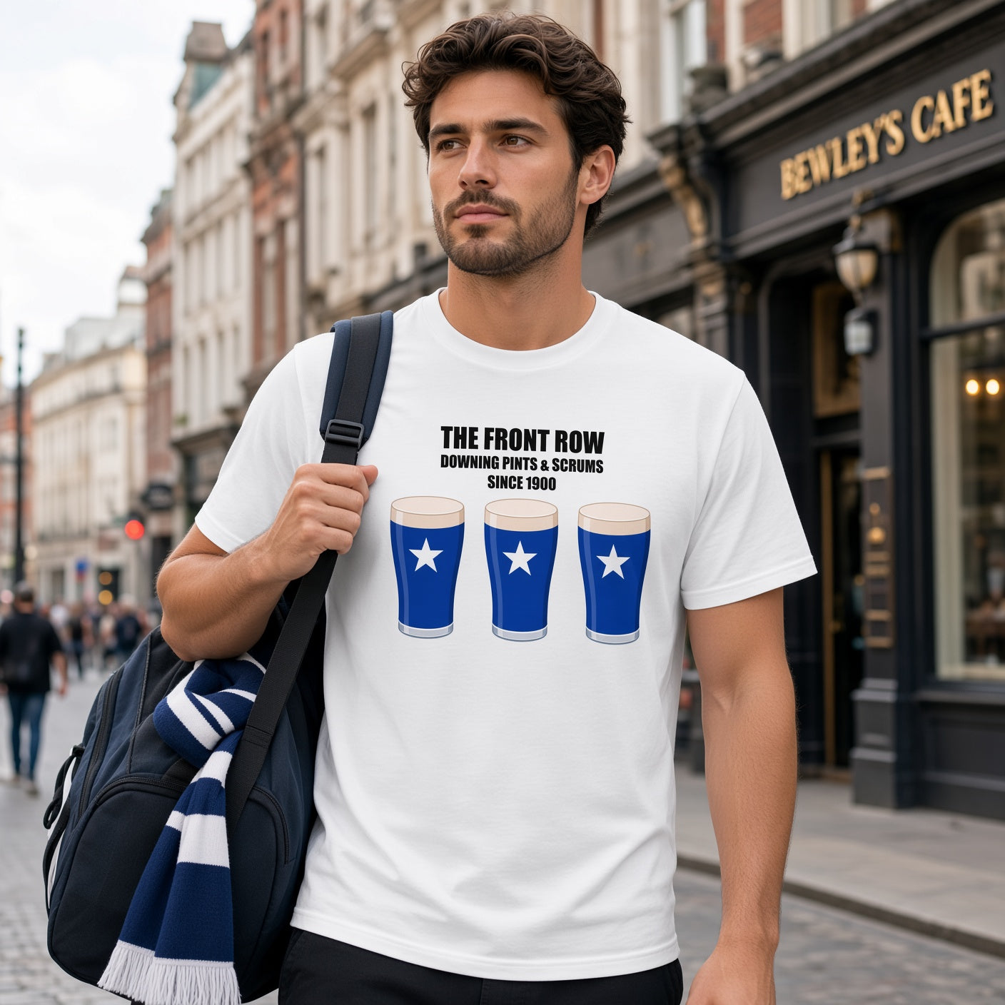 Male model wearing a white St Mary’s rugby t-shirt reading “The Front Row - Downing Pints & Scrums Since 1900” with three blue pint graphics featuring a white star, photographed on a town street for match day supporters
