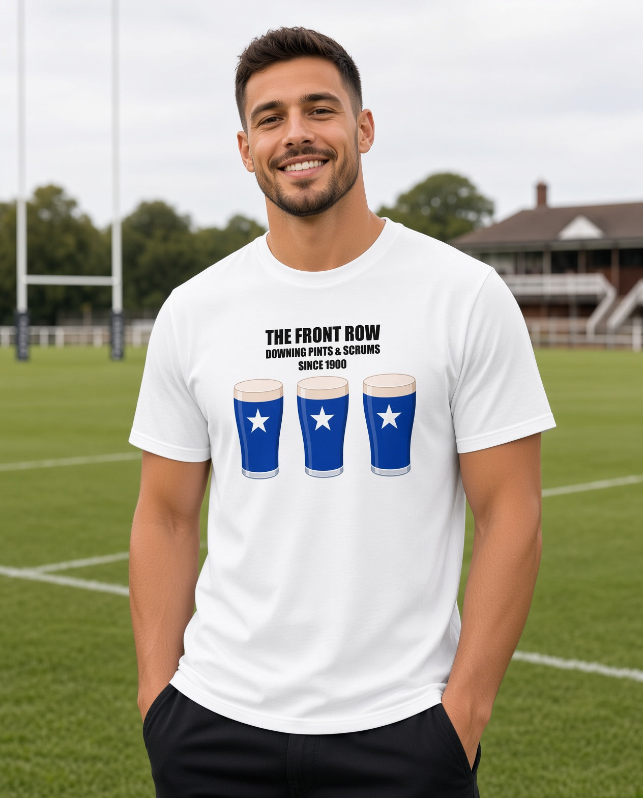Male model wearing a white St Mary’s rugby t-shirt reading “The Front Row - Downing Pints & Scrums Since 1900” with three blue pint graphics featuring a white star, photographed at a rugby ground for match day supporters